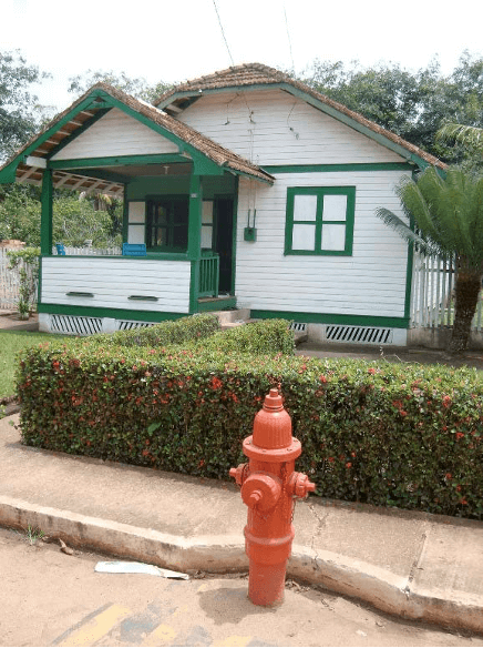 Casa de madeira branca com janelas verdes e hidrante vermelho na calçada, na Vila Americana de Belterra